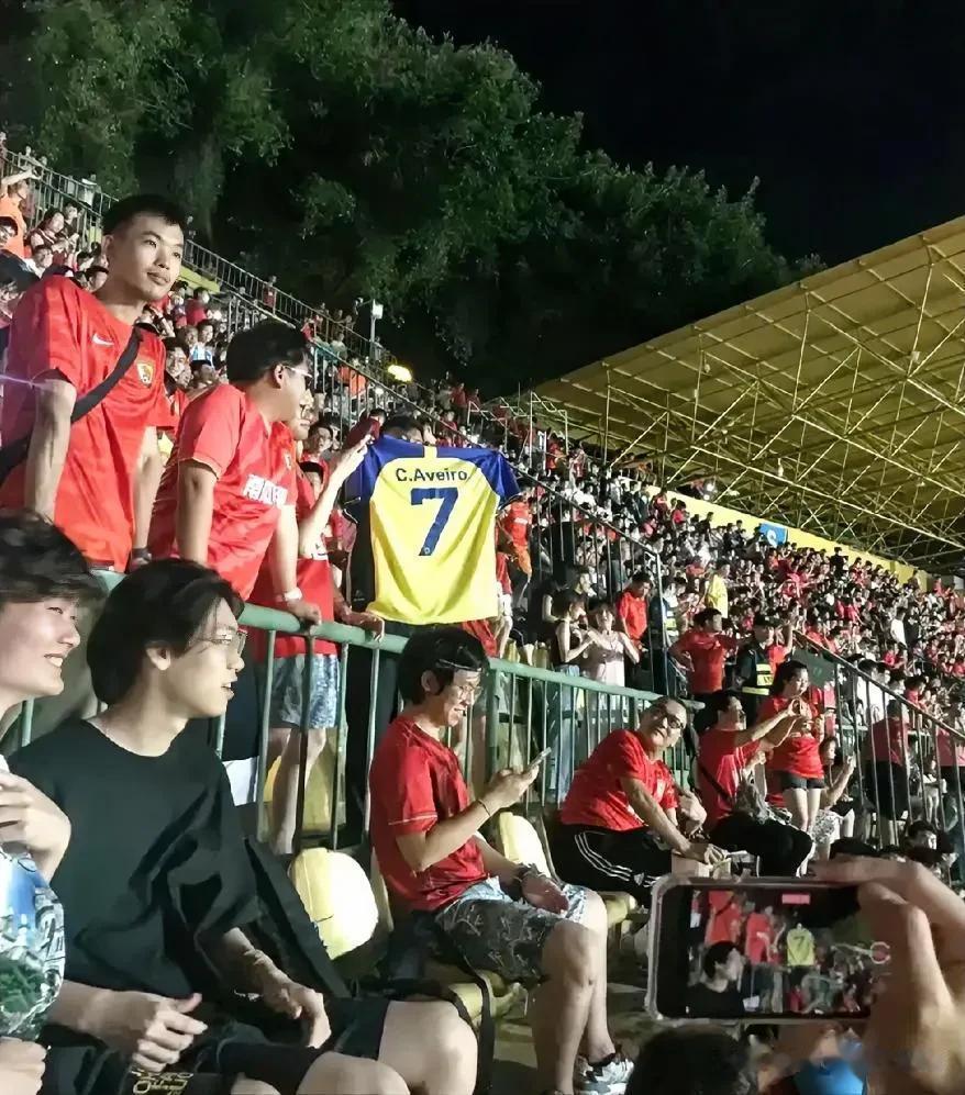  有观众在看台上高举利雅得胜利“C罗”球衣，然后广州队球员进球后，在场上做出了C(1)